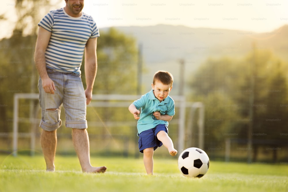 サッカー場でサッカーをしている幼い息子と若い父親