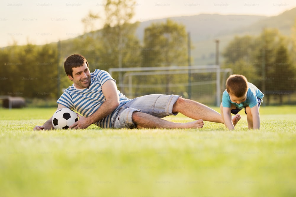 Pai jovem com seu filho pequeno jogando futebol no campo de futebol