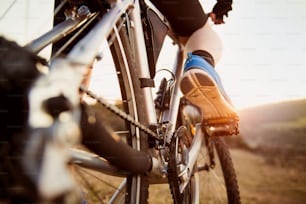 Detail of cyclist man feet riding mountain bike on outdoor trail in sunny meadow