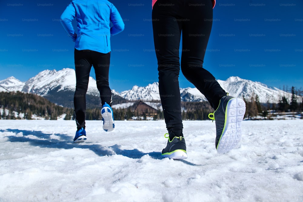 Young couple jogging outside in sunny winter mountains