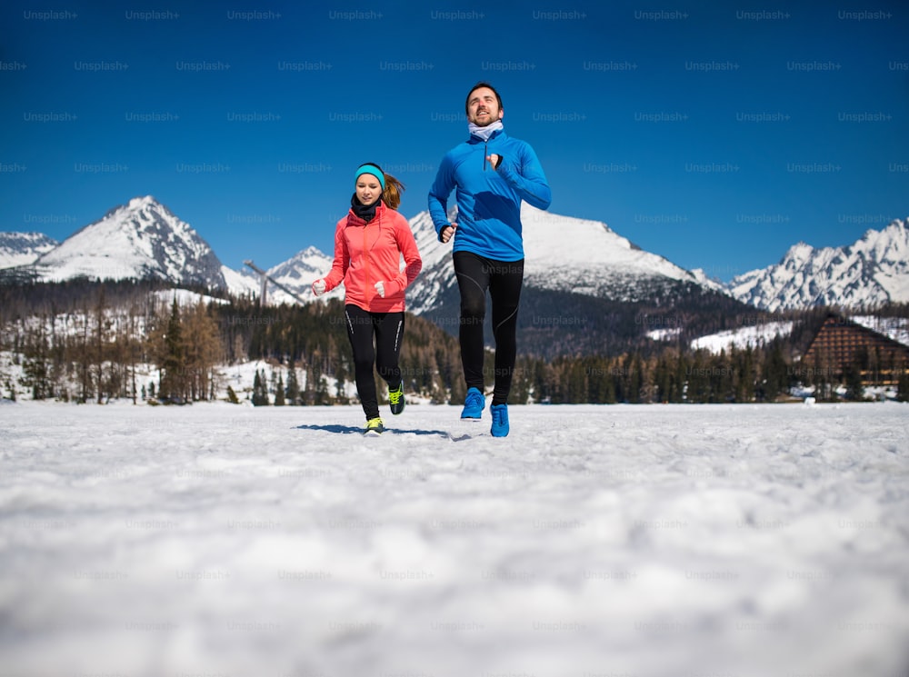 Casal jovem correndo ao ar livre em montanhas ensolaradas de inverno