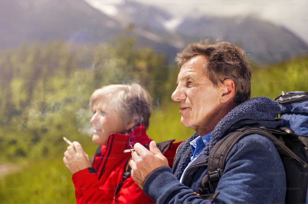 Casal de caminhantes seniores fumando durante a caminhada nas montanhas