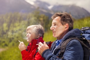 Coppia di escursionisti anziani che fumano durante la passeggiata in montagna
