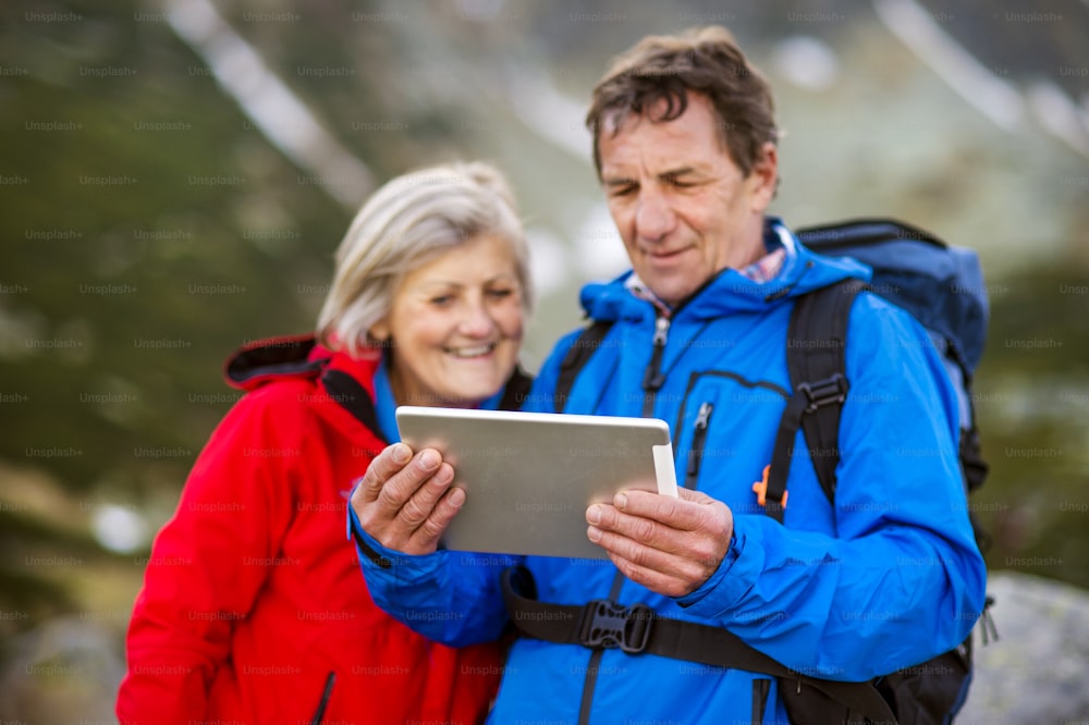 Pareja de excursionistas mayores usando la aplicación de viaje o el mapa en la tableta durante la caminata.