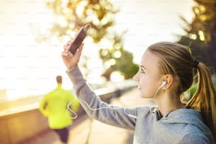 Young female runner is having break and taking selfie during the run in city on a quay