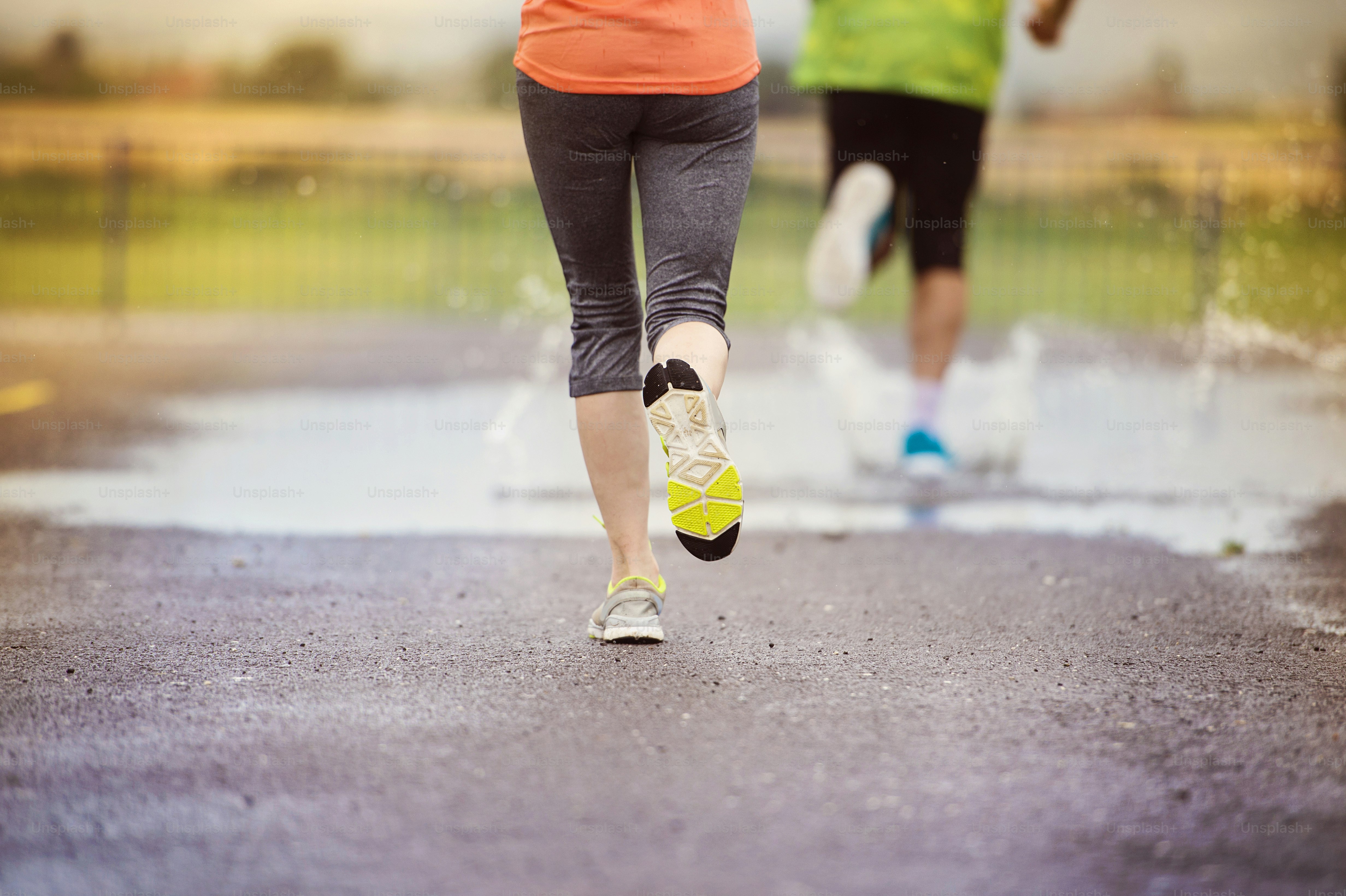 Jeune couple courant sur un terrain de sport asphalté par temps de pluie.  Détails des jambes et des chaussures de sport éclaboussant dans les flaques  d'eau. photo – Image de Pluie sur, image size:3000x1997