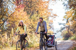 Beautiful young family with baby in jogging stroller cycling outside in autumn nature