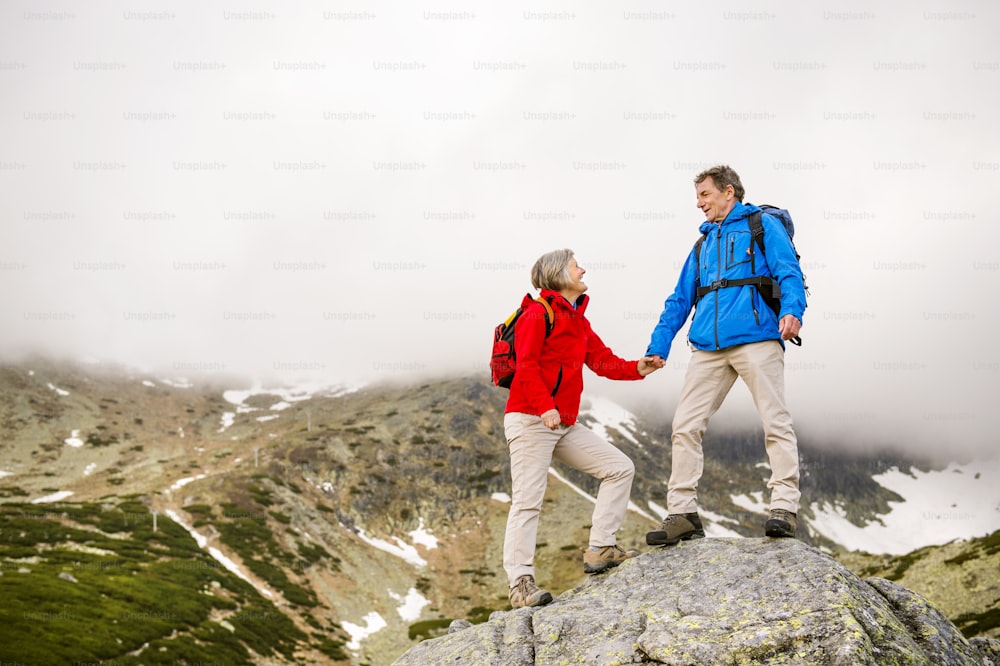 Coppia di turisti anziani che fanno escursioni, l'uomo sta aiutando la donna a raggiungere la roccia