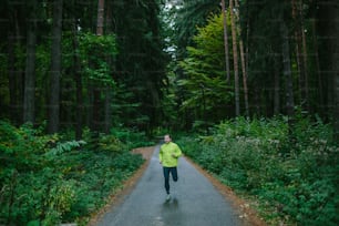 Man running and exercising for trail run on a path in an old green forest.
