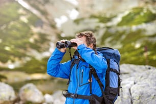 Senior hiker man enjoying the beautiful landscape view with binoculars during the hike