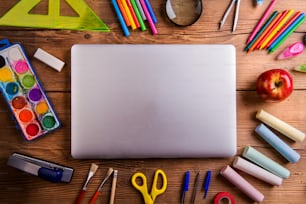 Desk with various school supplies and closed notebook  in the middle . Studio shot on wooden background, frame composition, empty copy space