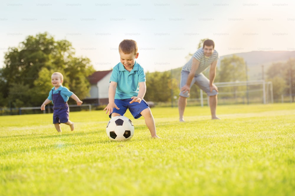 Giovane padre con i suoi figli piccoli che giocano a calcio sul campo da calcio