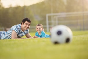 Young father with his little son having fun on football pitch