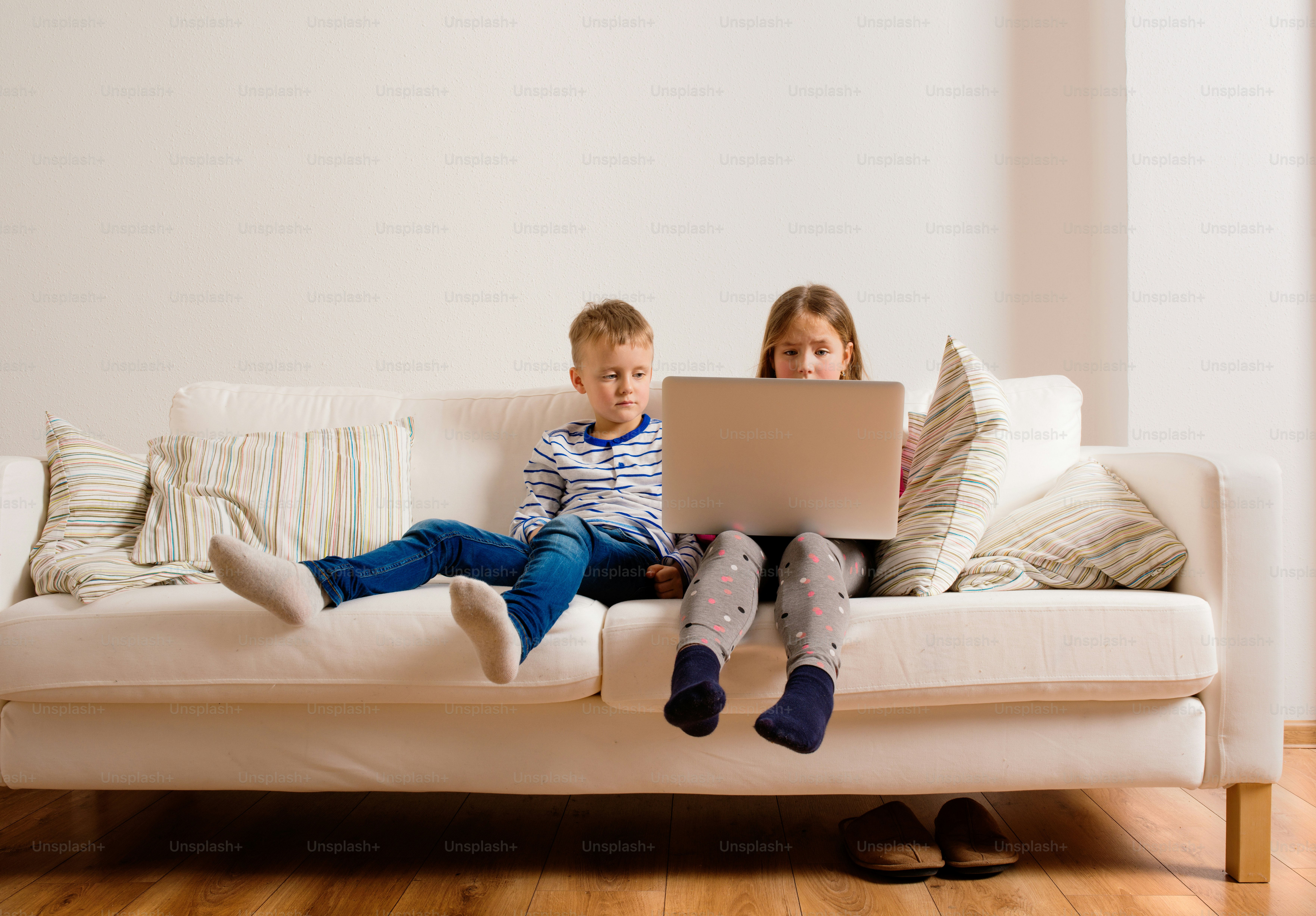 Little girl and boy sitting on sofa with a laptop computer at home. Happy children playing indoors using PC.