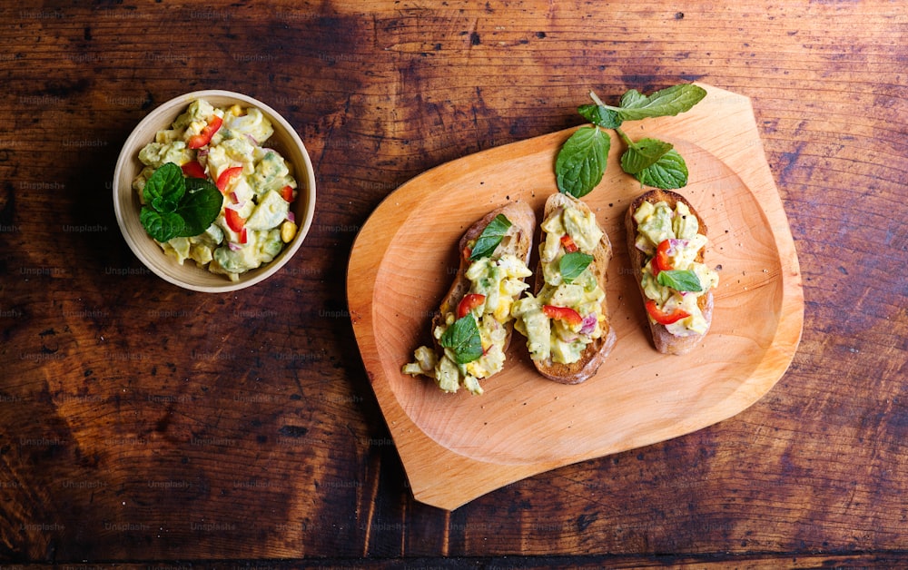 Spread made of avocado and other ingredients on slices of bruschetta. Studio shot on wooden background.