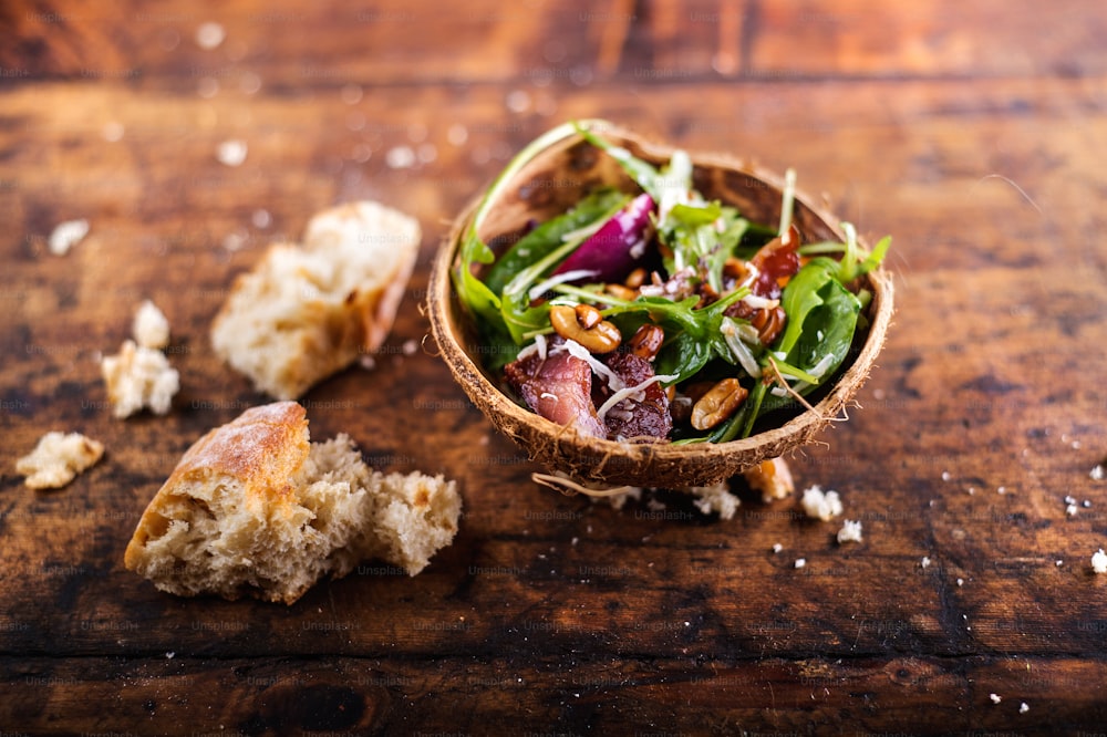 Rucola-Salat in einer Schüssel aus Kokosnussschale. Studioaufnahme auf hölzernem Hintergrund.