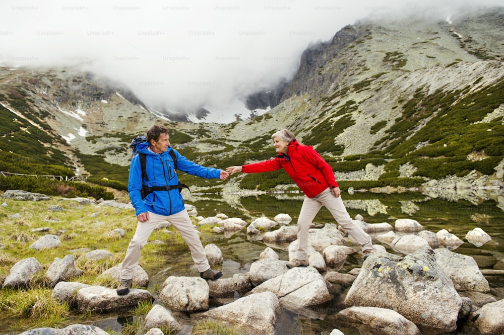 Senior tourist couple hiking at the beautiful mountains, tarn in the background