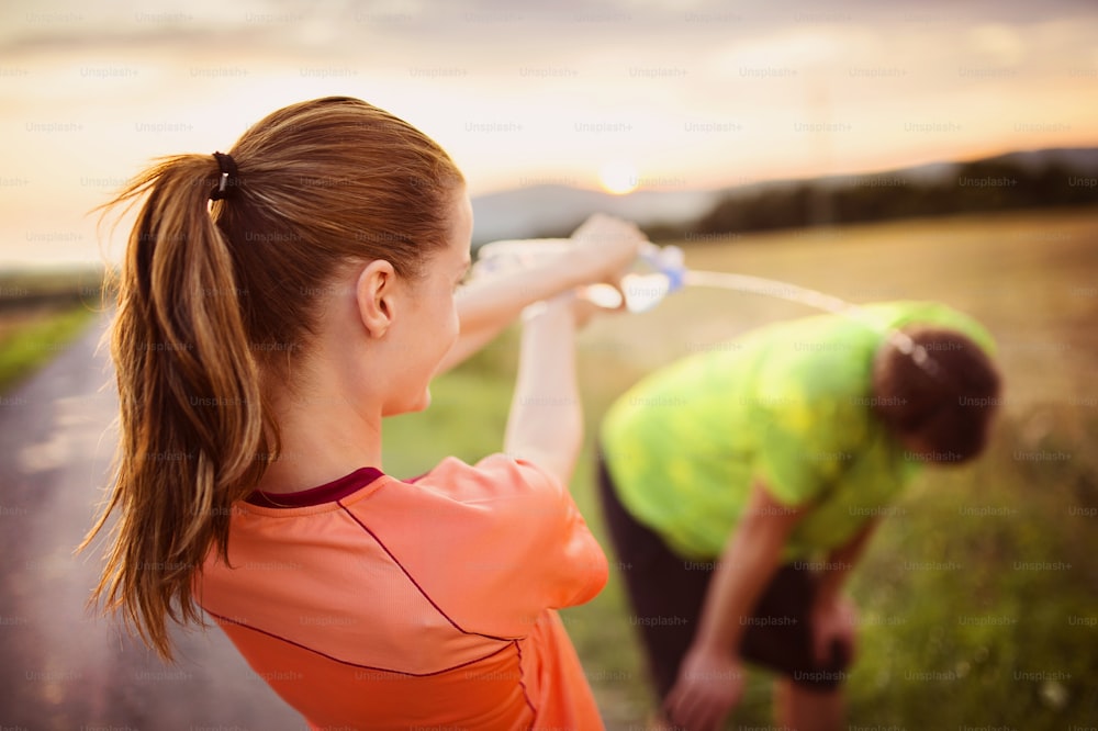 Cross-country trail running couple having water break at sunset