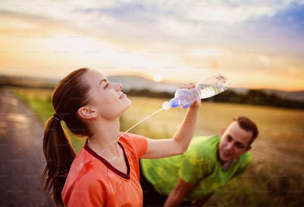 Cross-country trail running couple having water break at sunset