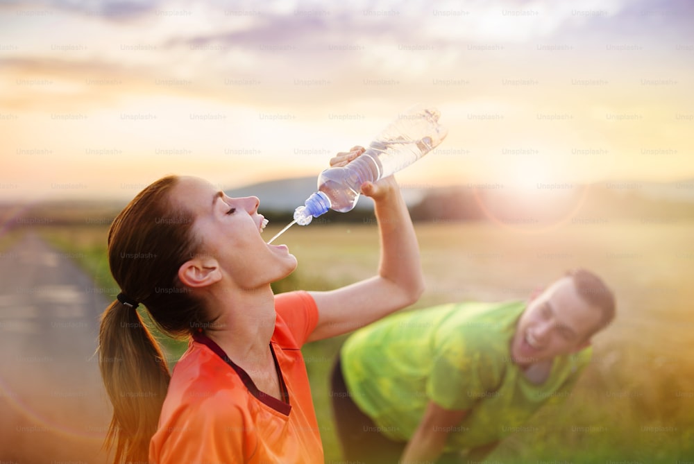 Cross-country trail running couple having water break at sunset