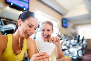 Two attractive fit women in a gym during a break with smart phone