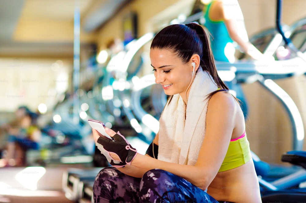 Atractiva mujer en forma en un gimnasio con teléfono inteligente contra una fila de cintas de correr