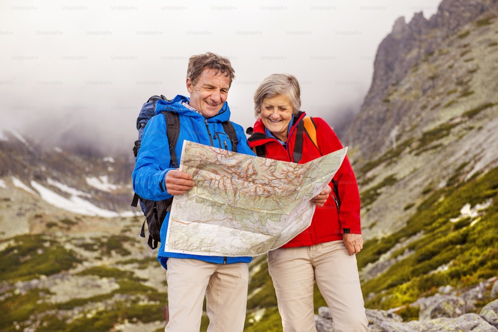 Couple de randonneurs âgés regardant la carte de randonnée pendant la randonnée dans de belles montagnes