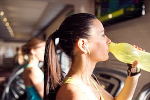 Donna attraente in forma in palestra sul tapis roulant che beve acqua dalla bottiglia
