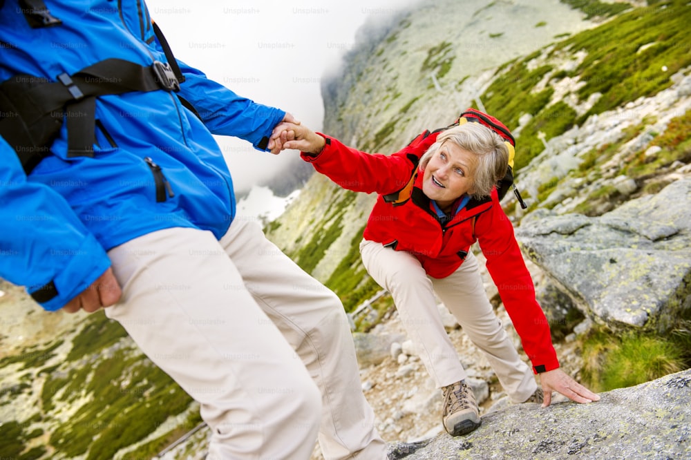Pareja de turistas mayores caminando, el hombre está ayudando a la mujer a llegar a la roca