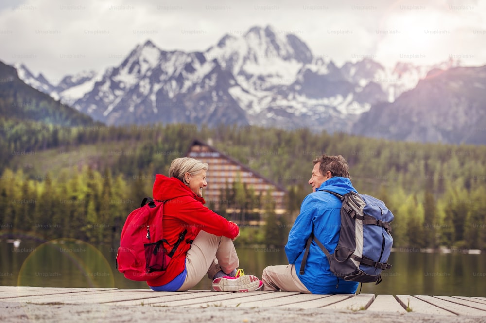 Senior hikers couple during the walk round the tarn in beautiful mountains, hills and hotel in background