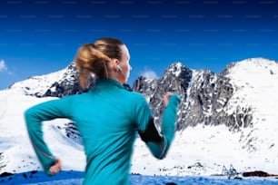Jeune femme faisant du jogging à l’extérieur dans les montagnes ensoleillées d’hiver