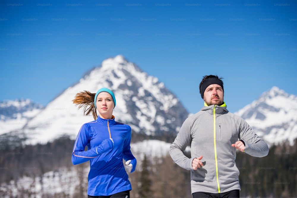 Jeune couple faisant du jogging à l’extérieur dans les montagnes ensoleillées d’hiver