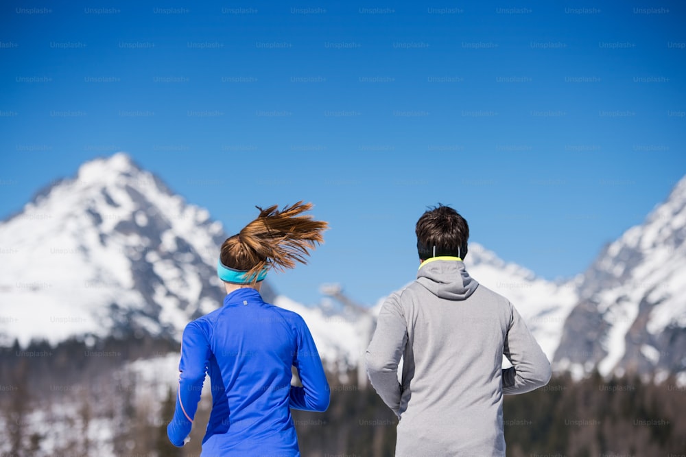太陽の光が降り注ぐ冬の山々で外をジョギングする若いカップル