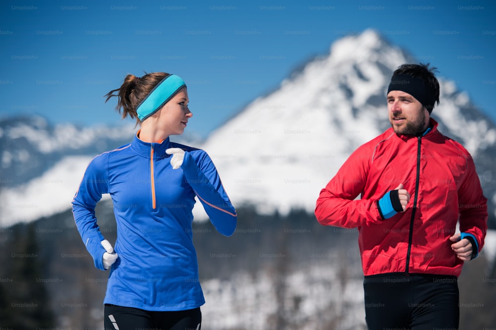 Young couple jogging outside in sunny winter mountains