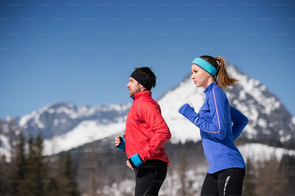 Young couple jogging outside in sunny winter mountains