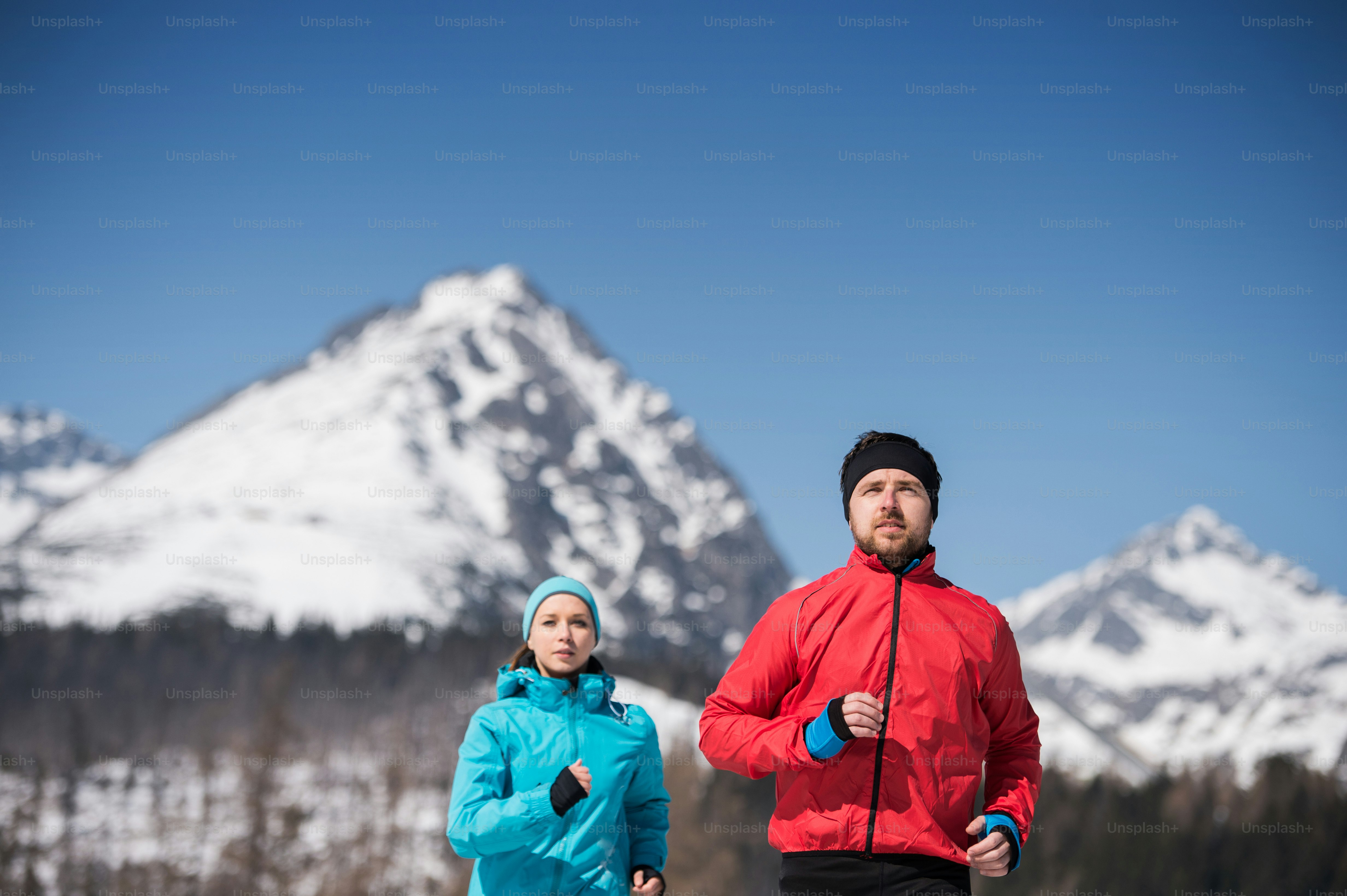 Jeune couple faisant du jogging à l’extérieur dans les montagnes ensoleillées d’hiver