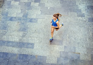 Hochwinkelansicht der jungen Läuferin, die auf dem gefliesten Bürgersteig der Altstadt in der Mitte joggt.
