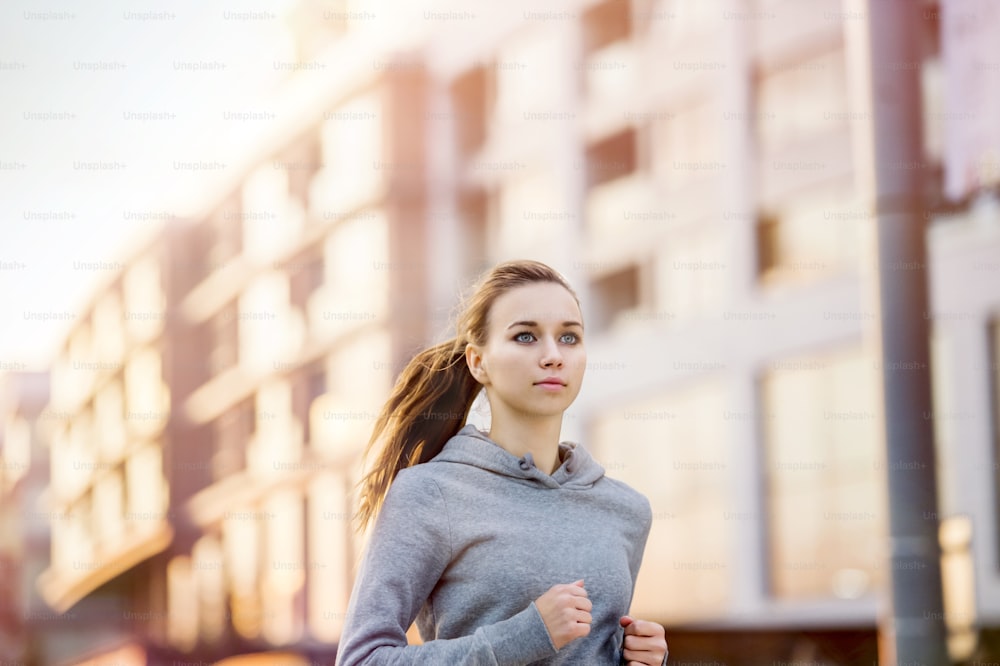 Giovane corridore femminile in felpa con cappuccio sta facendo jogging nella strada della città