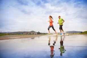 Young couple running on asphalt in rainy weather splashing in puddles.