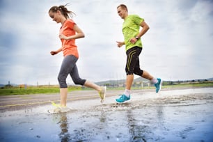 Young couple running on asphalt in rainy weather splashing in puddles.