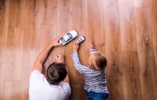 Unrecognizable father with his son playing with cars. Studio shot on wooden background.