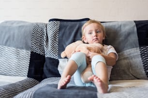 Cute little girl with her teddy bear at home sitting on sofa in living room