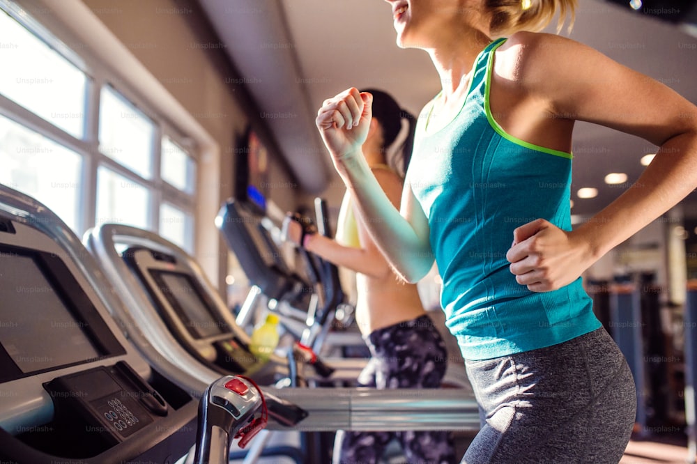 Two attractive fit women running in sports clothes on treadmills