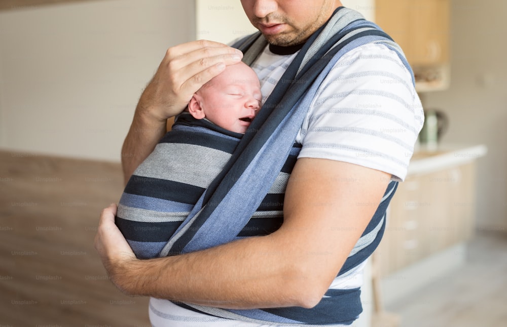 Gros plan d’un jeune père méconnaissable avec son fils nouveau-né en écharpe de portage à la maison