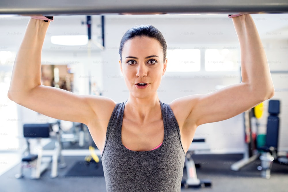 Close up de mulher atraente em forma na academia fazendo exercícios de braços em uma máquina