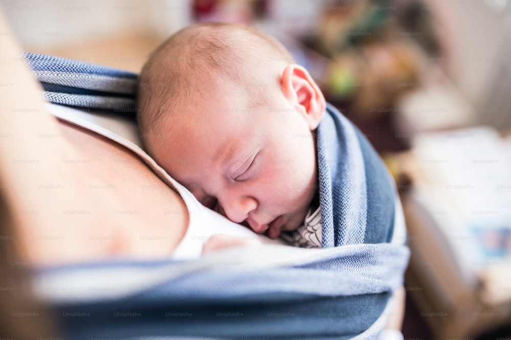 Primer plano de una madre joven irreconocible con su hijo recién nacido en cabestrillo en casa