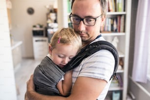 Young father with his daughter in baby carrier at home
