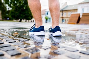町を走っている見分けのつかない男の足の接写、水たまり