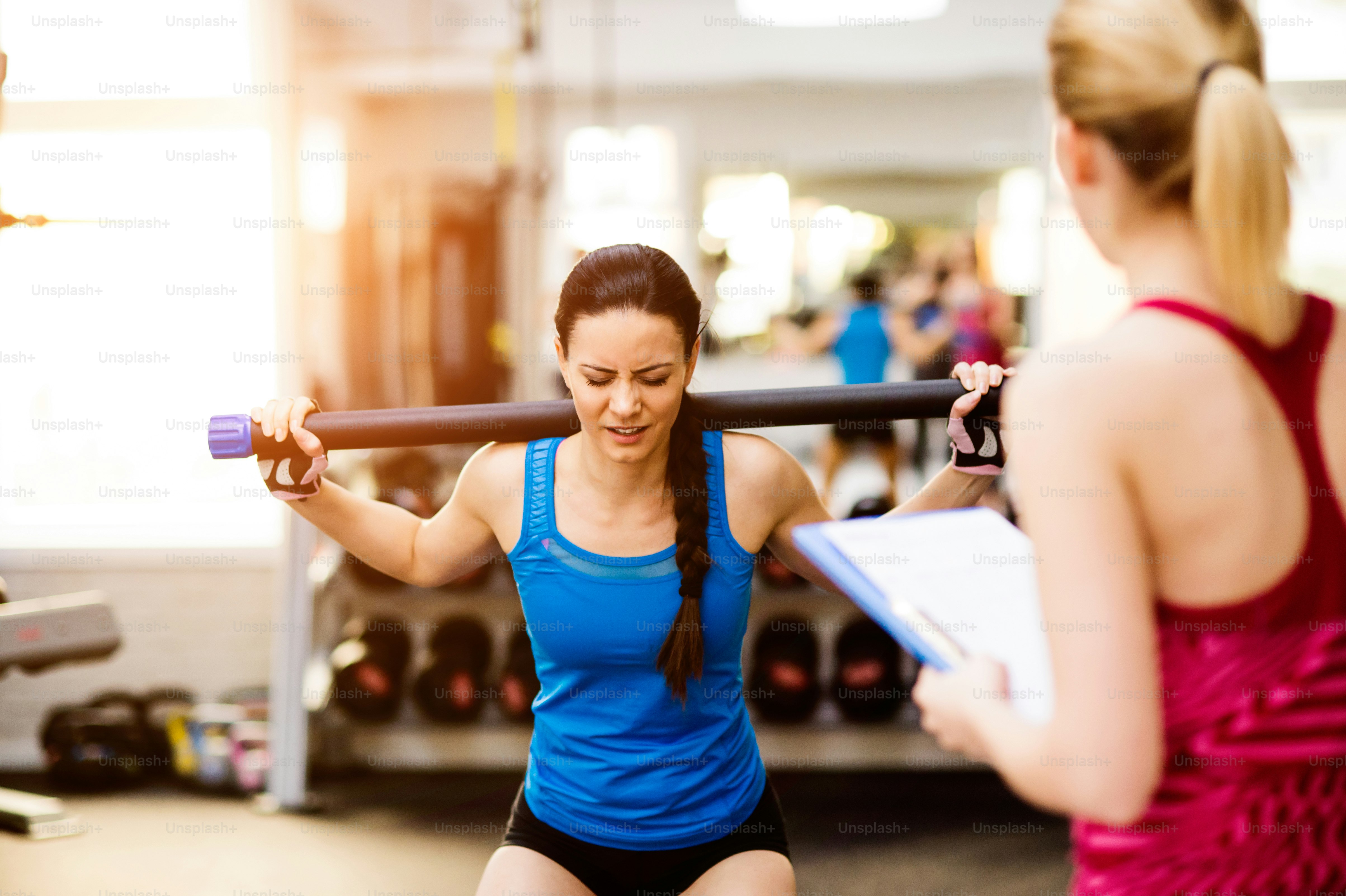 Close up of an attractive fit woman in blue singlet exercising in a gym with her personal trainer writing into exercise plan on clipboard