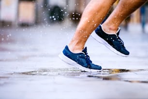 Close up of legs of unrecognizable man running in the town, puddle